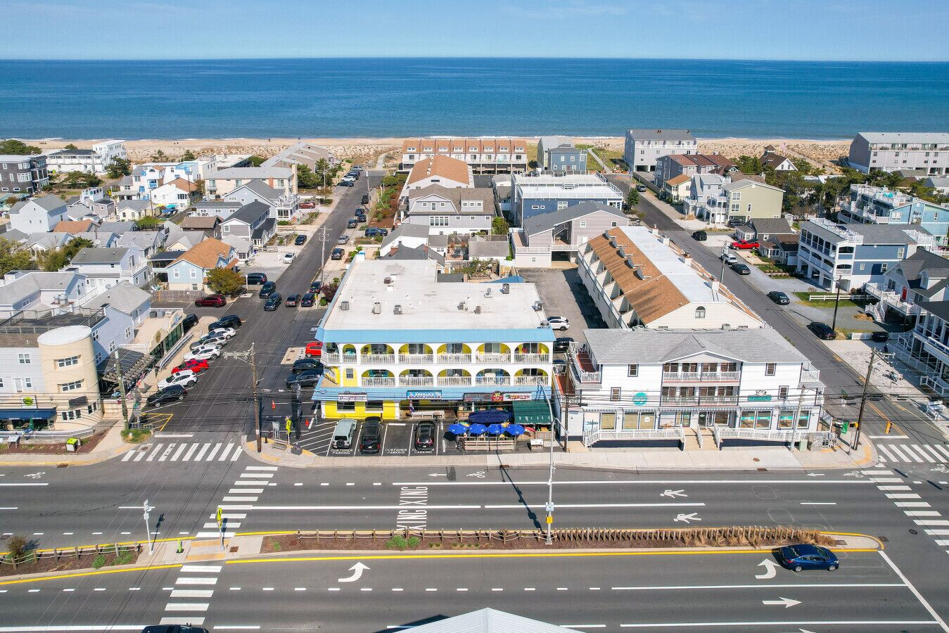 A coastal town with a prominent building featuring a blue and yellow facade, a crosswalk, and a view of the beach.