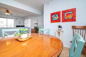 Un comedor con una mesa de madera, sillas y un jarrón de flores. Hay dos cuadros en la pared y un ventilador de techo.
