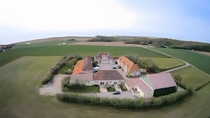 Luchtbeeld van een groot landgoed met meerdere gebouwen, een oprijlaan en omliggende velden.