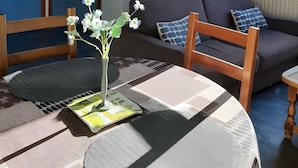 Een gezellige woonkamer met een bank, een tafel met een bloevas en een keukenhoek met een magnetron.