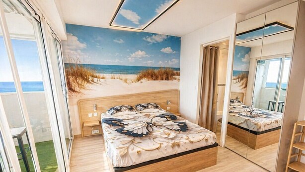 Quarto com cama, um espelho grande e vista para a praia por uma porta de vidro.