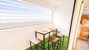 Um quarto com janela, uma mesa com bancos e um tapete verde.