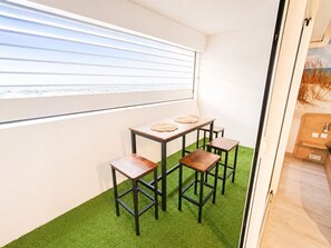 Ein Zimmer mit Fenster, einem Tisch mit Hocker und einem grünen Teppich.