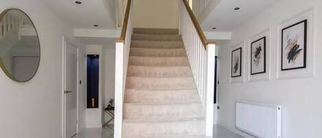 A staircase with a wooden handrail and beige carpet, leading to a landing with a mirror and framed artwork on the walls.