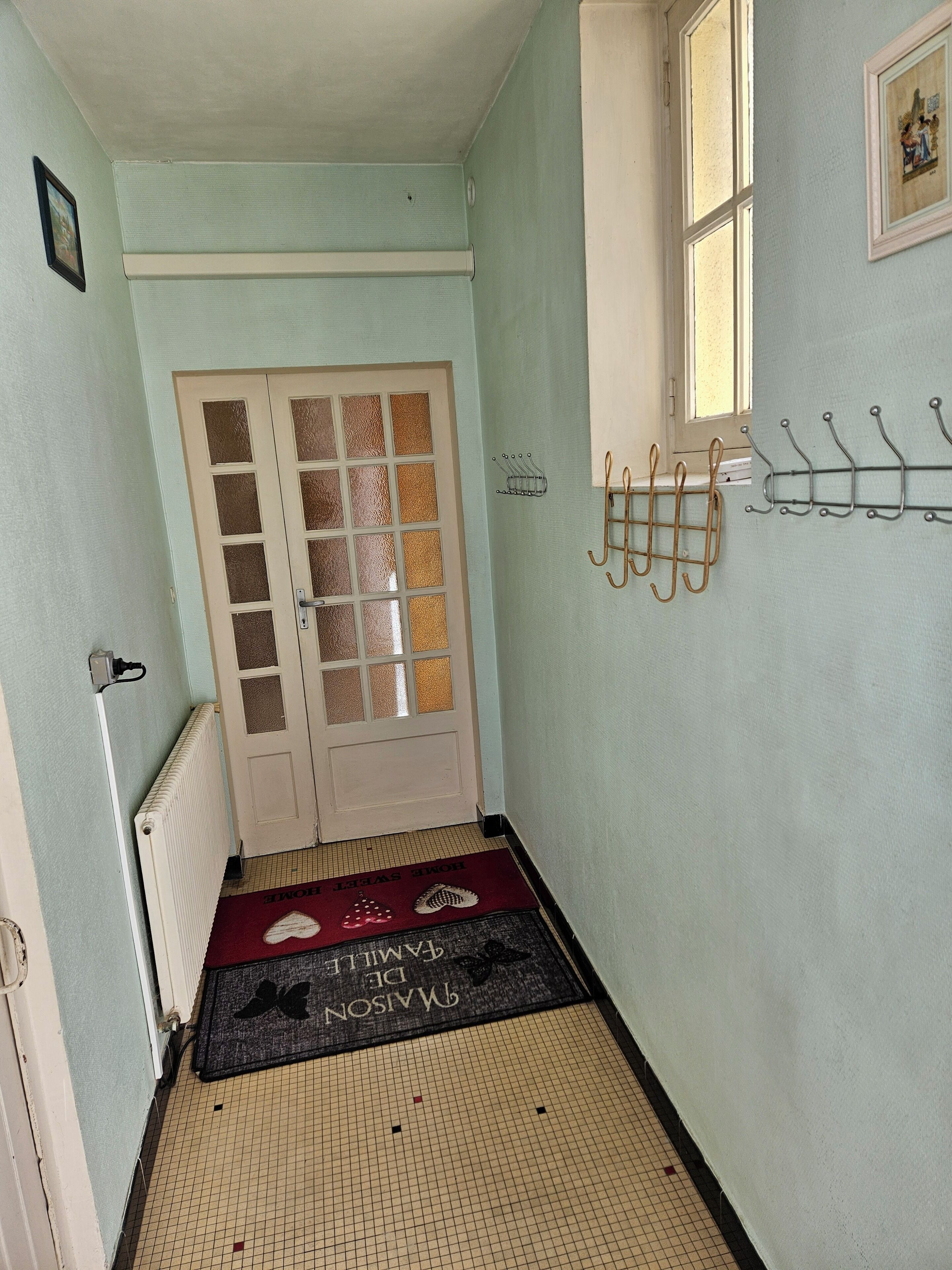 A hallway with a door, a radiator, a window, and a coat rack.