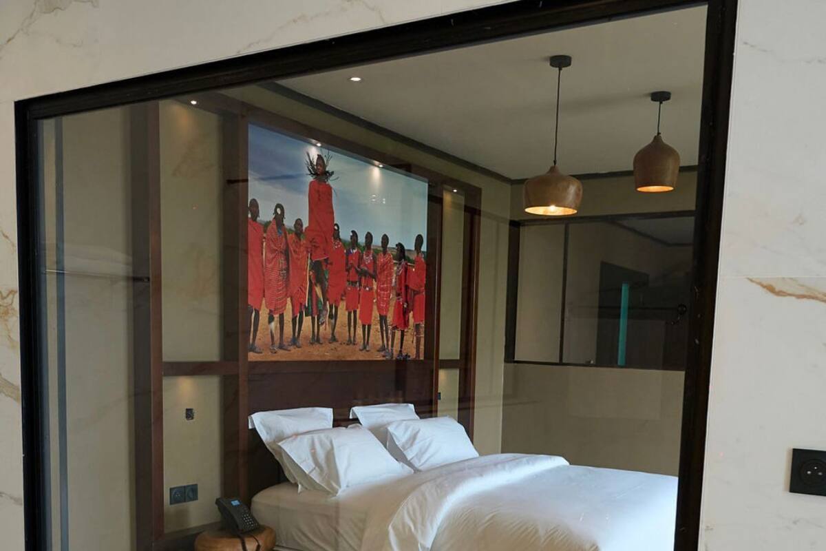 A modern hotel room with a large bed, a wooden floor, a small round table with a phone, and a painting of a group of people on the wall.