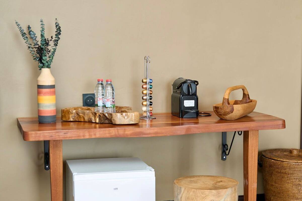 A compact kitchenette with a white refrigerator, a wooden coffee table, a woven basket, and a small wooden stool.