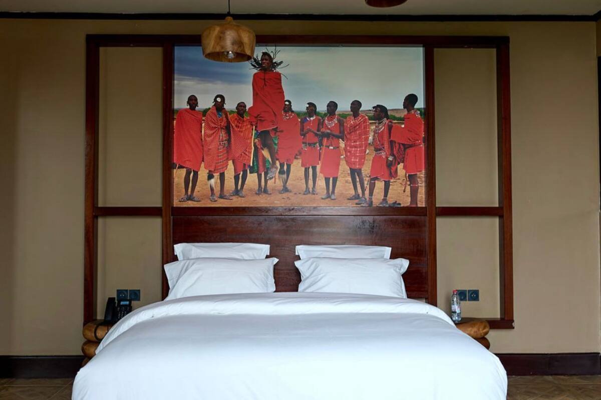 A large bed with white linens, a wooden headboard, and a painting of a group in traditional attire on the wall behind it.