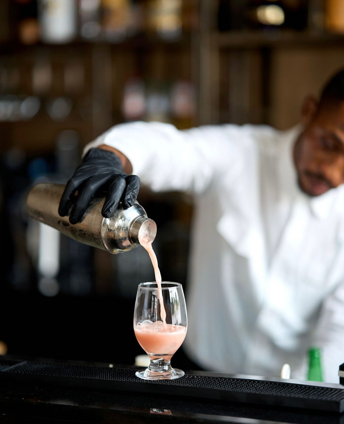 A bartender pouring a pink drink into a glass.