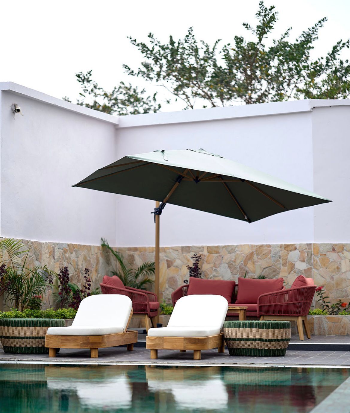 Un área junto a la piscina con sillones de descanso y una sombrilla grande.