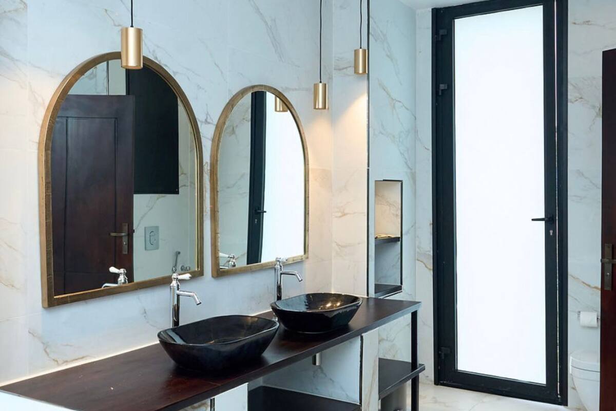 A modern bathroom with a marble floor, two sinks with black bowls, and large mirrors with gold frames.