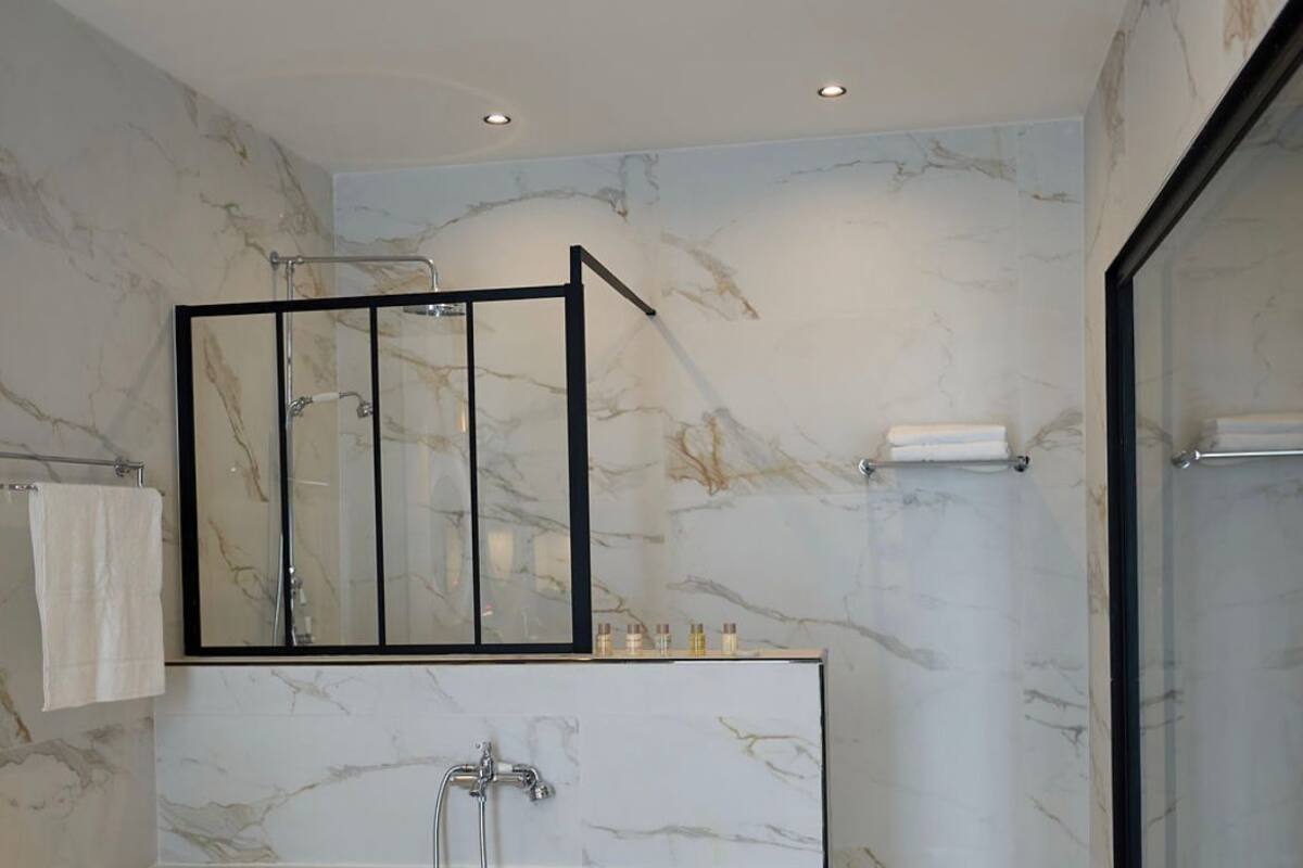 A modern bathroom with a freestanding bathtub, a glass-enclosed shower, and marble walls.