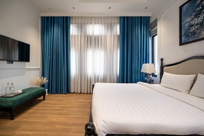 A hotel room with a large bed, a bedside table with a lamp, a flat-screen TV mounted on the wall, and a bench with a tray of bottles and glasses. - An Dinh La Maison by Teky House (Thuan Hoa)