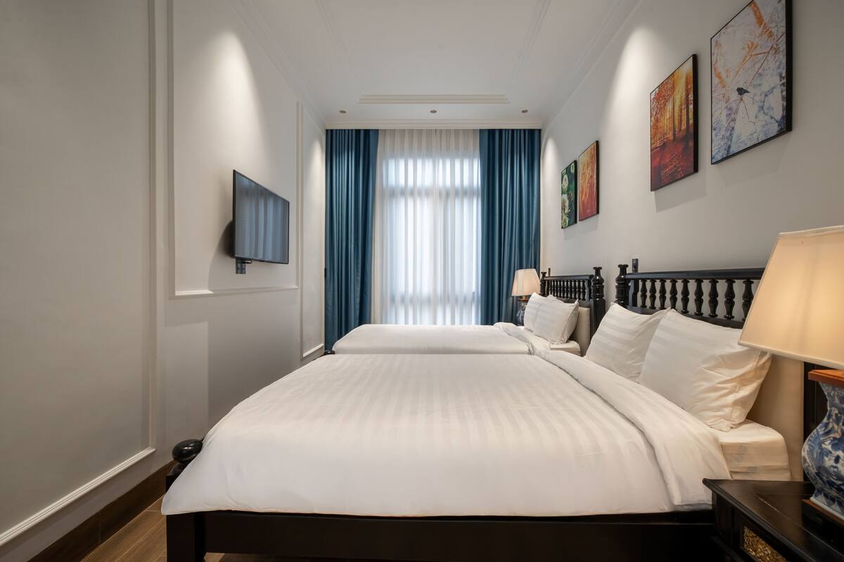 A hotel room with a large bed, a TV mounted on the wall, and a window with blue curtains.