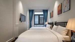 Habitació d'hotel amb un llit gran, televisió penjada a la paret i una finestra amb cortines.