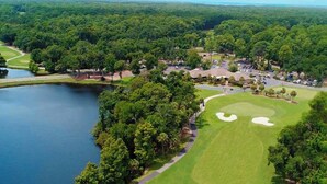 Vista aerea di un campo da golf con un lago, circondato da alberi fitti e edifici residenziali.