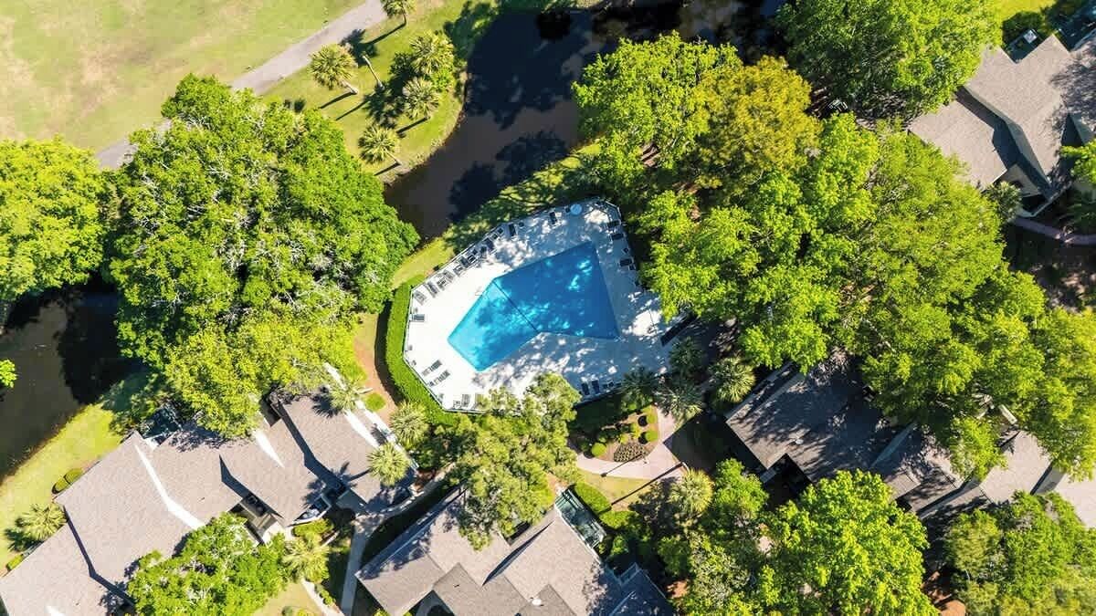 An aerial view of a residential area with a swimming pool surrounded by lush greenery and houses.