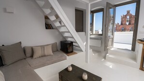 Una sala de estar moderna con un sofá, una mesa de centro, una chimenea y una escalera que lleva a un balcón con vistas a un edificio rojo.