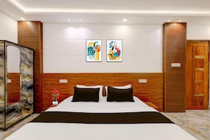 A hotel room with a bed, two wall-mounted artworks, a wooden headboard, a wardrobe, and a mirror.