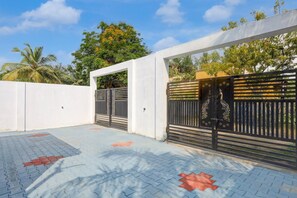 A gated entrance with a white wall and a black gate with decorative elements.