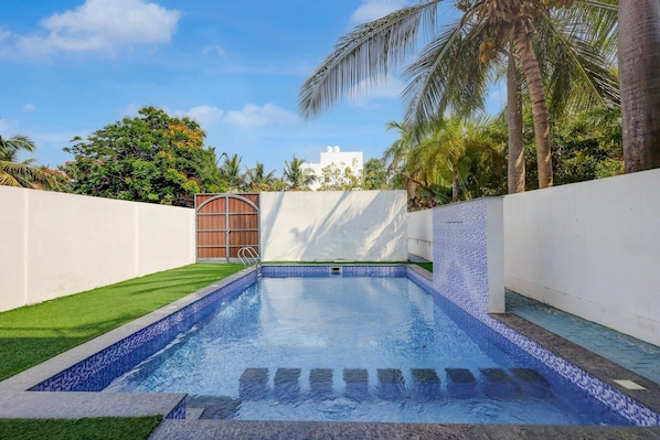 A swimming pool with tiled edges, surrounded by a white wall and a grassy area.