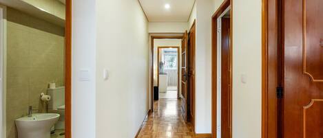 Un pasillo con puertas de madera, un baño con baldosas y un suelo con estampado tipo espiga.