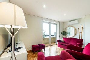 Ein modernes Wohnzimmer mit einer roten Sofagarnitur, einer Stehlampe und einem großen Fenster mit Blick auf die Stadt.