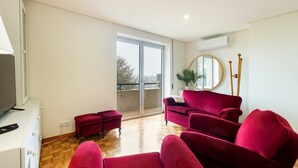 A spacious living area with a red sofa, a red armchair, and a small red ottoman. There is a large window providing a view of the outdoors. - GuestReady - Charming Braga retreat (Braga)