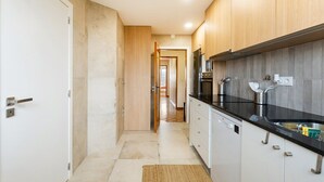 A narrow kitchen with wooden cabinets, a black countertop, and a tiled backsplash. - GuestReady - Charming Braga retreat (Braga)