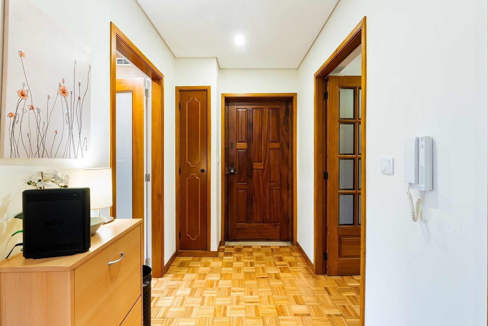 Um corredor com portas de madeira, um telefone na parede e uma mesa com um computador.