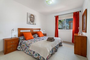 Un dormitorio con cama, mesita de noche, cómoda, ventana con cortinas y un cuadro de Buda en la pared.