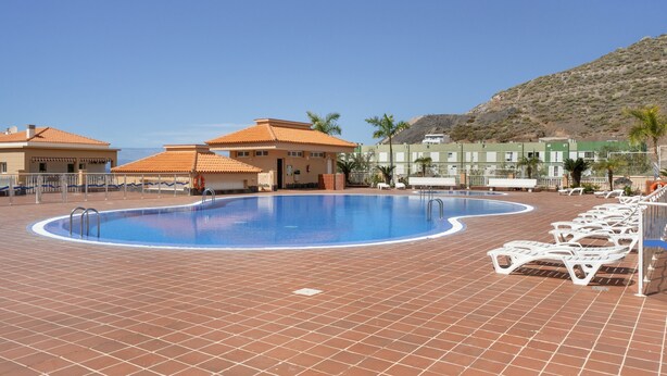Une piscine avec des chaises longues, un bâtiment doté d’un toit en tuiles et un paysage montagneux en arrière-plan.