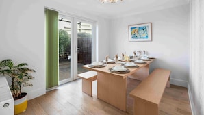 A dining area with a table set for four, a bench, a potted plant, and a ceiling light fixture. - Sea Palm By My Getaways (Lancing)