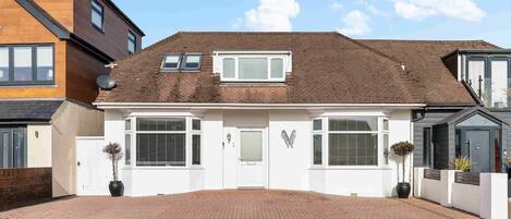 Ein modernes, zweistöckiges Haus mit Pflasterweg, heller Fassade und einem kleinen Garten mit Topfpflanzen.