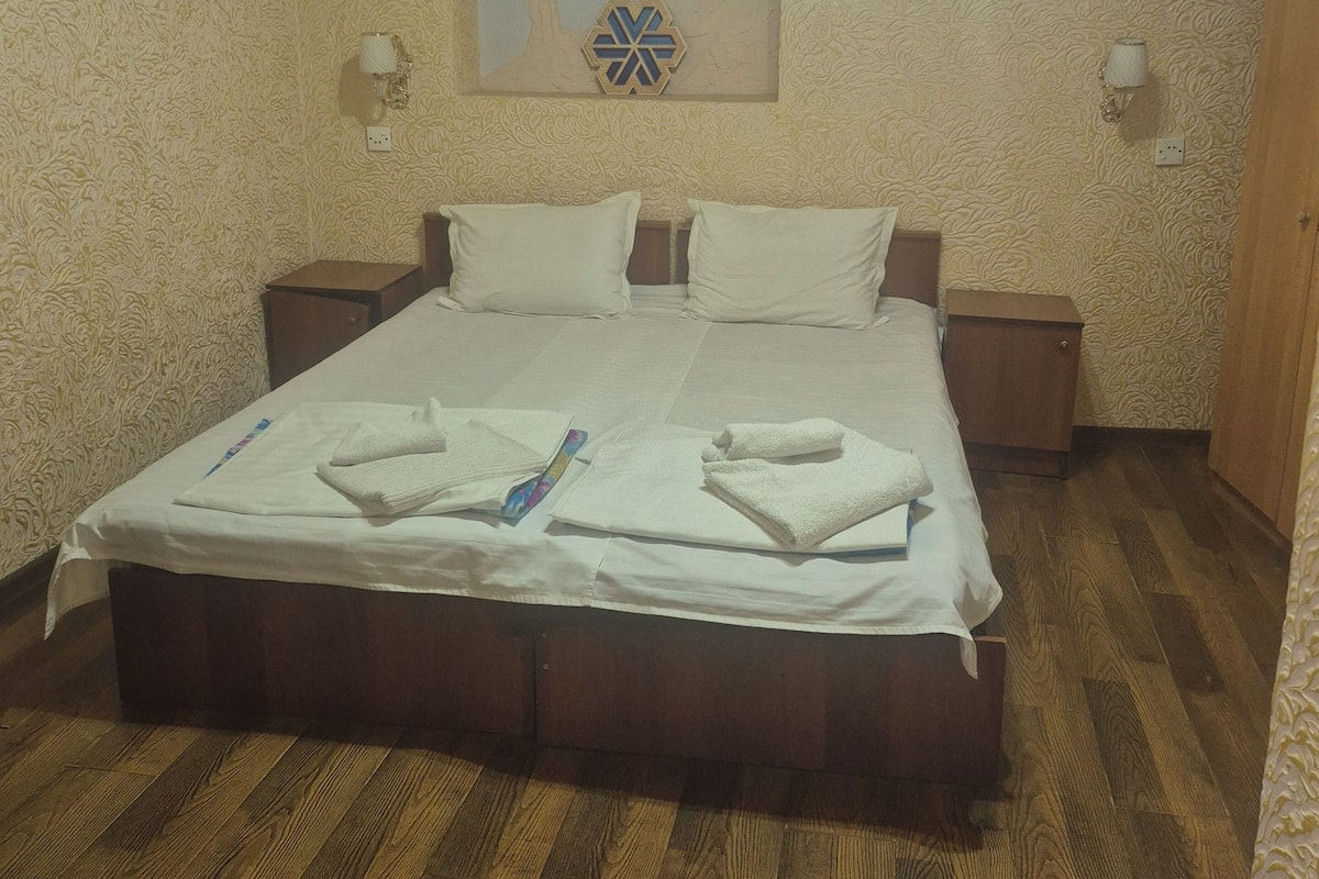 A bedroom with a large bed, two bedside tables, a wall-mounted light fixture, and a decorative wall piece.