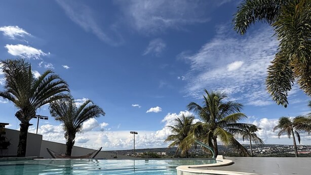Una piscina cristalina con bordes de azulejos, rodeada de palmeras y un cielo despejado.