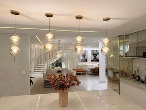 Un interior moderno con una zona de comedor central, una escalera y una cocina con paredes de vidrio.