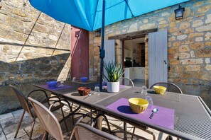 An outdoor dining area with stone walls, metal chairs, and a table set with bowls and cutlery.