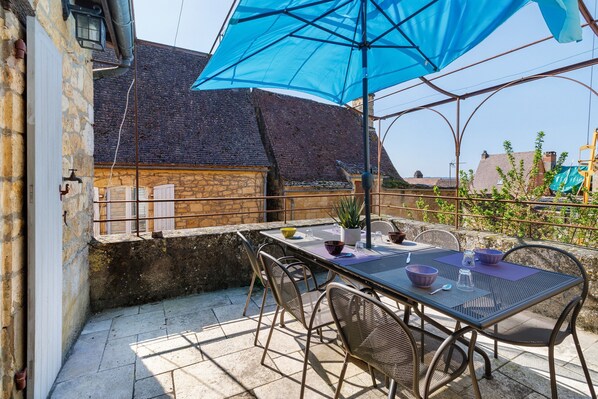 An outdoor patio with a table and chairs, a blue umbrella, and a stone wall.