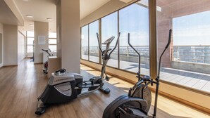 Una palestra moderna con macchinari cardio e ampie finestre che offrono vista sulla città.