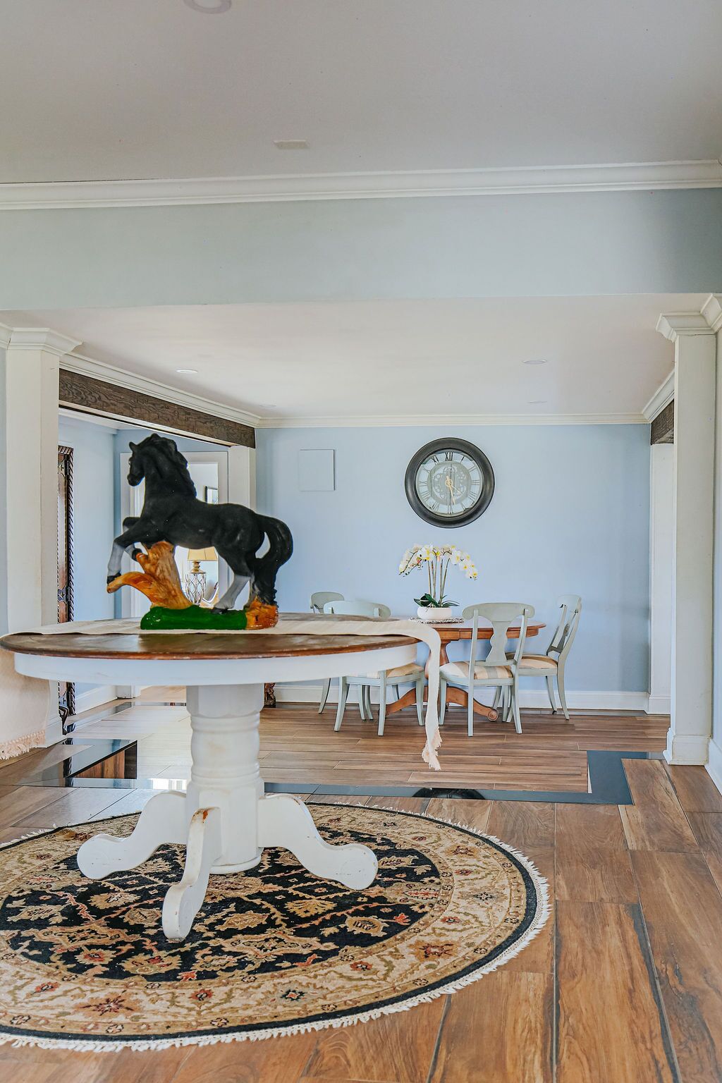 Un coin repas comprenant une table ronde, des chaises, un tapis, une horloge au mur et une sculpture de cheval.