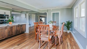 Une cuisine spacieuse dotée de meubles en bois, une table à manger avec des chaises et une grande fenêtre laissant entrer la lumière naturelle.