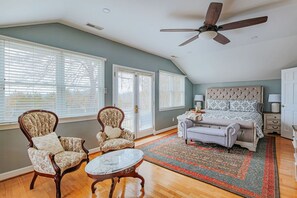 A bedroom with a bed, two armchairs, a coffee table, and a ceiling fan.