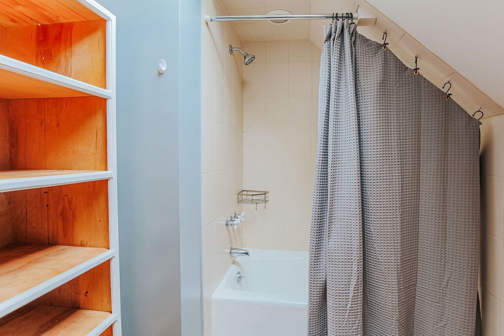 A bathroom with a bathtub, shower curtain, and wooden shelves.