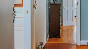 Un couloir avec un plancher en bois, une porte blanche, un meuble en bois et une petite statue.