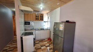 A compact kitchen with white cabinets, a microwave, a refrigerator, and a stove. - Family Cabin in Rapel Lake (Santiago, the goats)