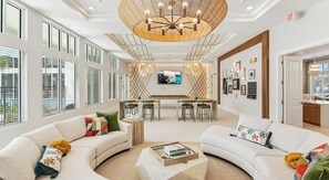 A spacious hotel lobby with a large chandelier, a TV mounted on the wall, and a dining area with a bar. - Landing | Stylish 2BD, Gym, Pool (Palm Bay)