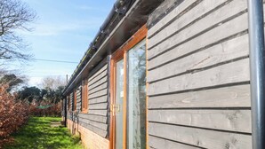 A modern house with a wooden exterior, a glass door, and a brick foundation. - Bluebell Cottage (Maidstone)