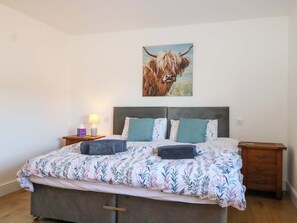 Une chambre à coucher avec un lit, deux tables de chevet, une lampe et un tableau représentant une vache accroché au mur.