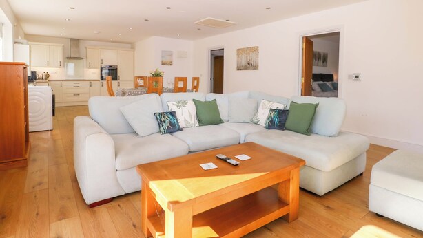A modern living room with a sectional sofa, a wooden coffee table, and a kitchen in the background. - Bluebell Cottage (Maidstone)